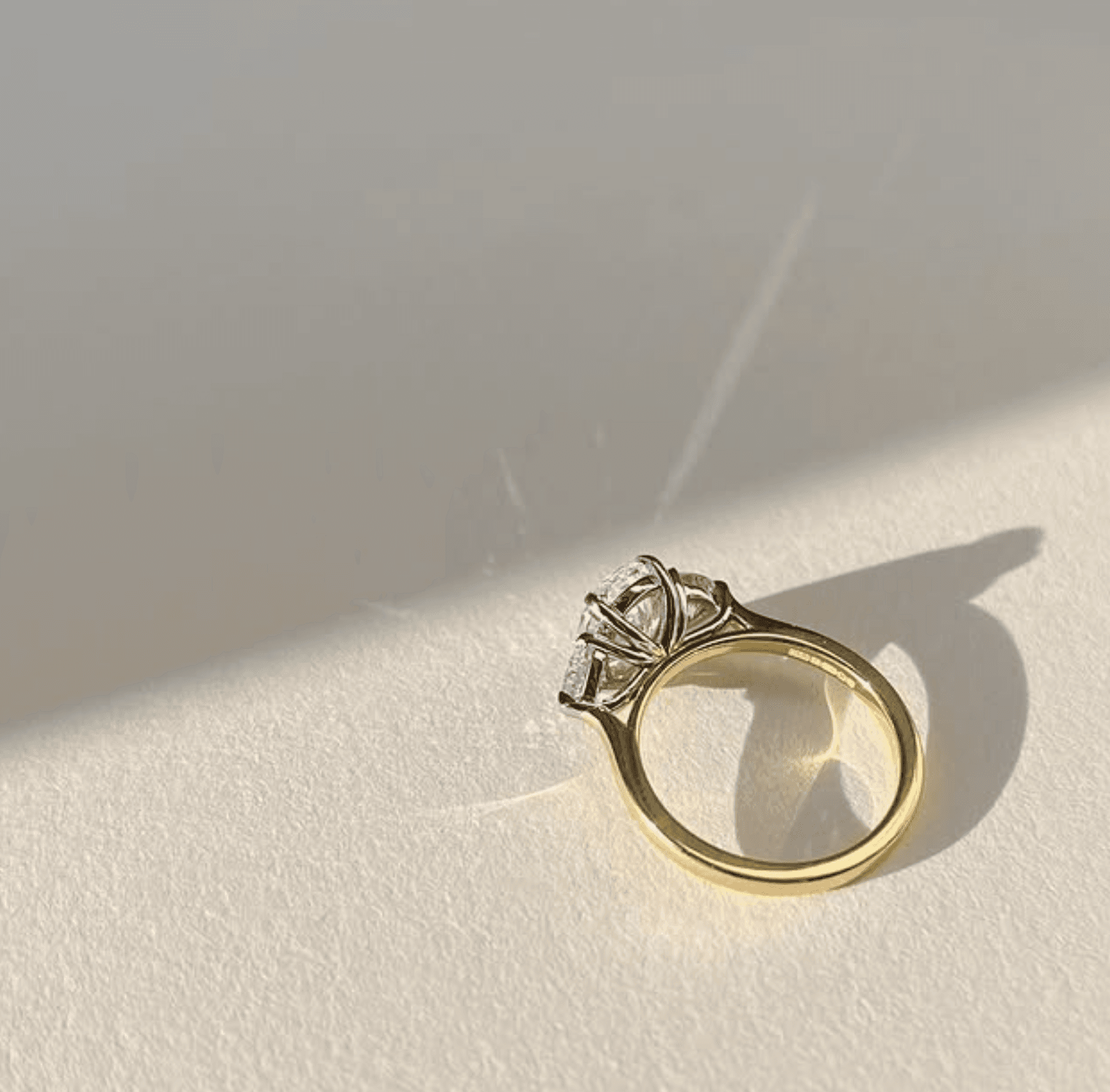 Three-stone diamond engagement ring in 18ct yellow gold casting a precise shadow across cream cartridge paper in window light