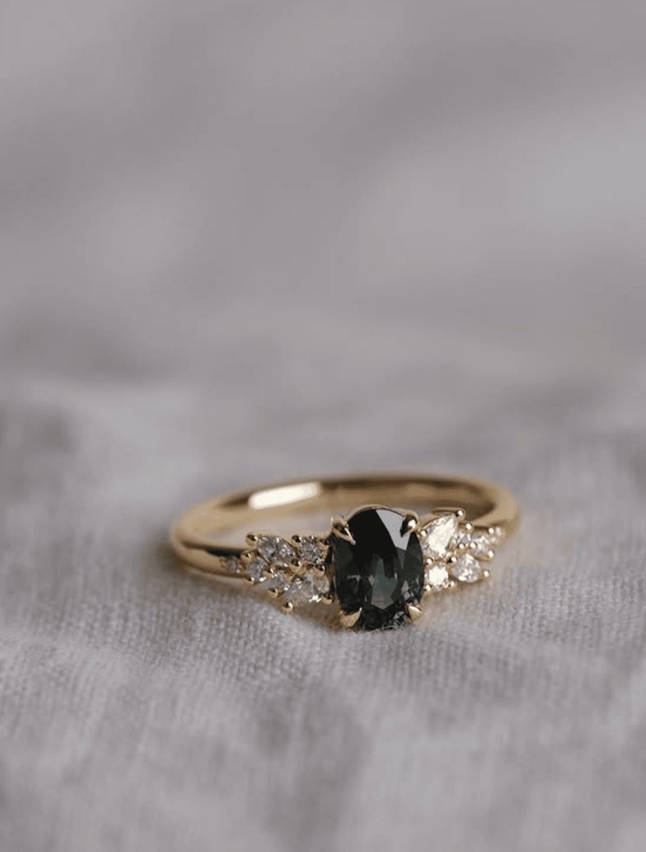 Teal oval sapphire ring with scattered diamond shoulders photographed on a soft grey linen cloth